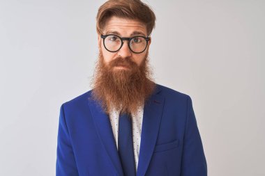 Genç, kızıl saçlı, takım elbiseli ve gözlüklü bir iş adamı izole edilmiş beyaz bir arka plan ve yüzünde ciddi bir ifade var. Basit ve doğal bir şekilde kameraya bakıyorsun..