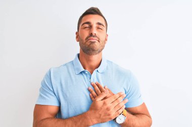 Soyutlanmış arka plan üzerinde mavi tişört giyen, elleri göğsünde, gözleri kapalı ve yüzünde minnet dolu bir jest olan genç yakışıklı bir adam. Sağlık kavramı.