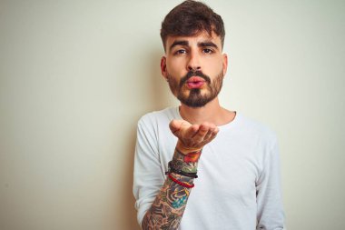 İzole edilmiş beyaz arka plan üzerinde duran tişörtlü genç bir adam kameraya bakıp havada öpücükler savuruyor. Güzel ve seksi. Aşk ifadesi.