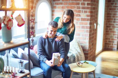 Mutlu ve kendinden emin gülümseyen genç bir çift. Evde Noel süslemeleri yapan sürpriz bir kadın var.