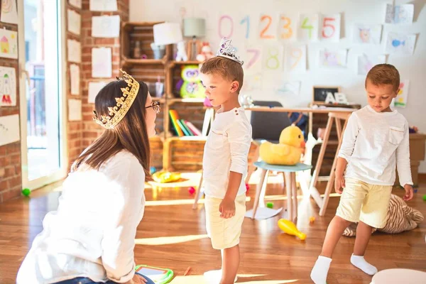 Beautiful teacher and toddlers playing with king crown around lots of toys at kindergarten