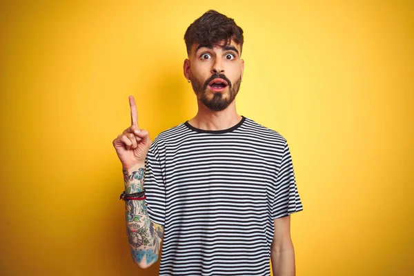 Mladý Muž Tetováním Pruhovaném Tričku Stojící Nad Izolovaným Žlutým Pozadím — Stock fotografie