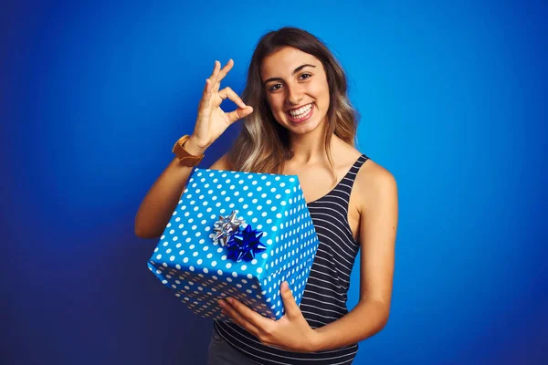 Young Woman Holding Birthday Present Blue Isolated Background Doing Sign — Stock Photo, Image