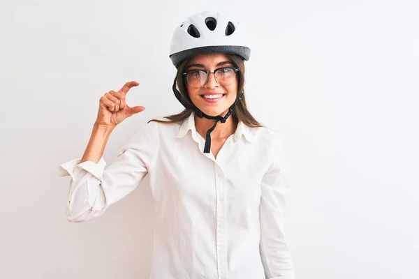 Beautiful businesswoman wearing glasses and bike helmet over isolated white background smiling and confident gesturing with hand doing small size sign with fingers looking and the camera. Measure concept.
