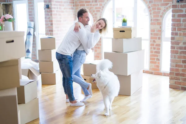 Young beautiful couple with dog hugging at new home around cardboard boxes