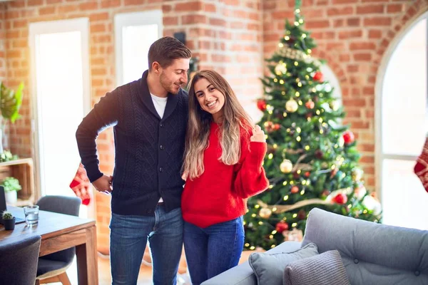 年轻漂亮的夫妇面带微笑 既快乐又自信 在家里站着抱着圣诞树 — 图库照片