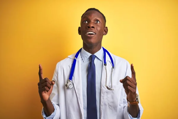 アフリカ系アメリカ人の医者の男を身に着けています聴診器を身に着けています独立した黄色の背景驚きと驚きを見上げ指と腕を上げて — ストック写真