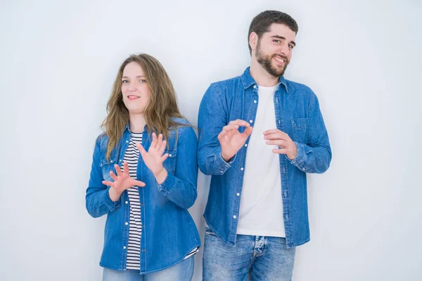 Young beautiful couple standing together over white isolated background disgusted expression, displeased and fearful doing disgust face because aversion reaction. With hands raised. Annoying concept.