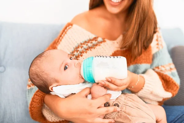 若い美しい女性と自宅でソファの上で彼女の赤ちゃん 新生児と母親は 哺乳瓶を使用して快適な飲料牛乳をリラックスして休憩 — ストック写真