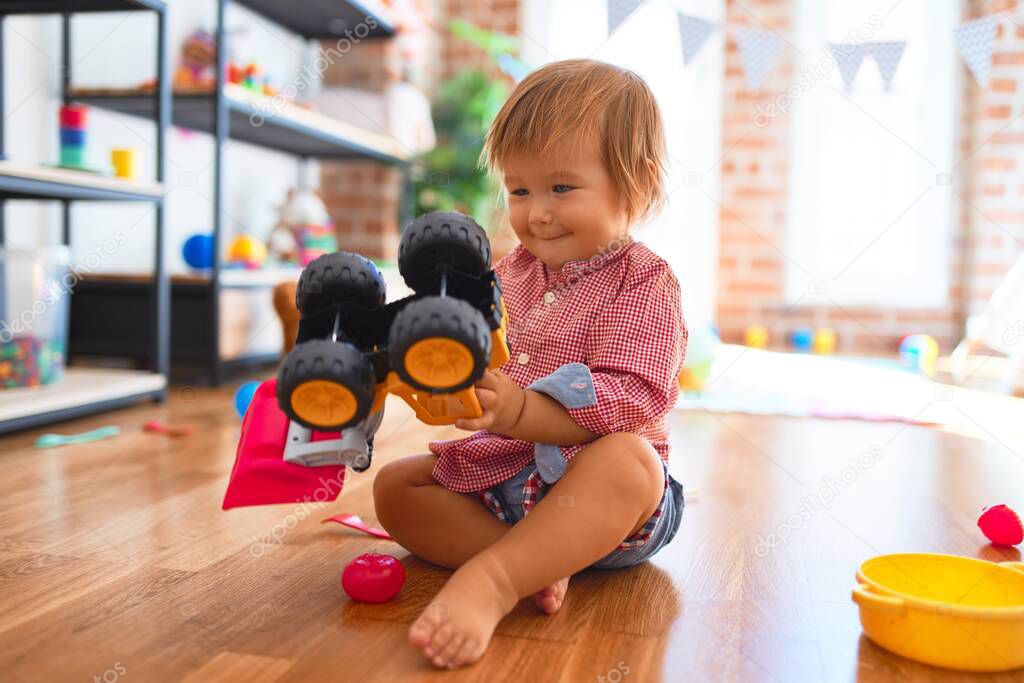 Adorable toddler playing with tractor. Smiling with happy face around lots of toys at kindergarten