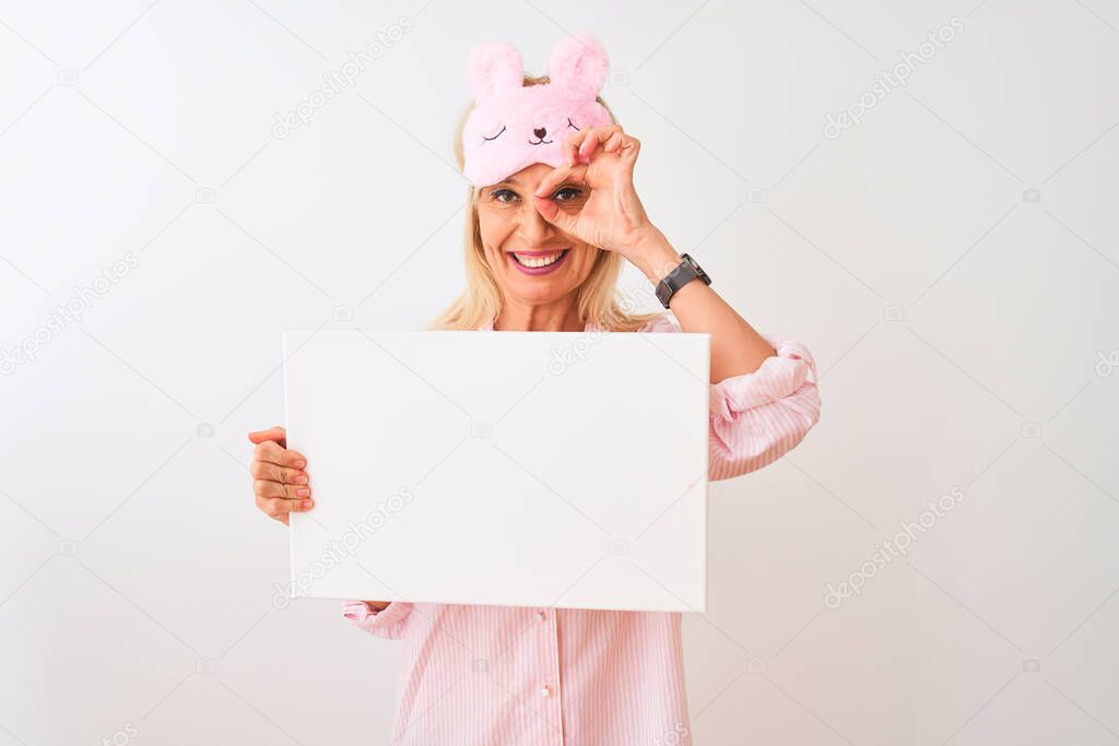 Middle age woman wearing sleep mask pajama holding banner over isolated white background with happy face smiling doing ok sign with hand on eye looking through fingers