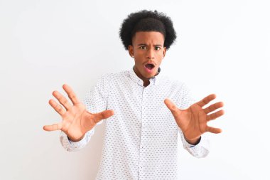 Zarif bir gömlek giyen genç Afro-Amerikalı adam izole edilmiş beyaz arka planda duruyor korku ifadesinden korkuyor ve dehşete düşüyor. El hareketlerini durdur, şok içinde bağır. Panik konsepti.