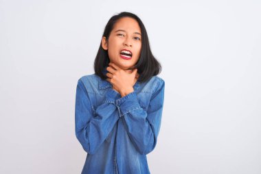 Genç, güzel, kot gömlek giyen Çinli bir kadın izole edilmiş beyaz arka planda durup bağırıyor ve boğuluyor çünkü acı verici bir boğulma var. Sağlık problemi. Boğulma ve intihar konsepti.