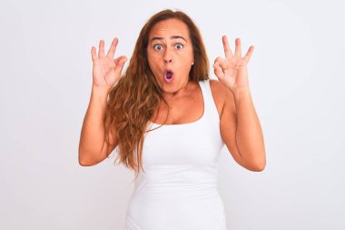 Beyaz soyutlanmış arka planda duran orta yaşlı olgun bir kadın şaşırmış ve şok olmuş bir şekilde parmaklarıyla onay sembolü yapıyor. Çılgın ifade