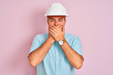 Güvenlik kaskı takan genç mimar pembe arka planda dikiliyor. Ağzını yanlışlıkla ellerle kapatıyor. Gizli konsept.