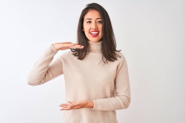 Balıkçı yaka kazak giyen güzel Çinli kadın izole edilmiş beyaz arka plan üzerinde duruyor. Ellerinde büyük ve büyük beden işareti, ölçü sembolü var. Kameraya bakıp gülümsüyor. Ölçüm konsepti.