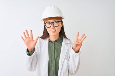 Genç Çinli mühendis kadın, izole edilmiş beyaz arka planda gözlük takıyor ve 8 numaralı parmaklarıyla işaret ederken kendinden emin ve mutlu bir şekilde gülümsüyor..