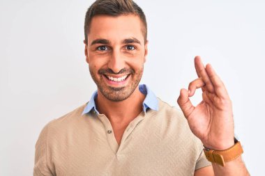 Soyutlanmış arkaplanda zarif tişörtler giyen genç yakışıklı adam tamam işareti yapıyor, mükemmel bir sembol.