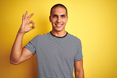Sarı izole edilmiş arka planda çizgili tişört giyen yakışıklı genç adam el ve parmaklarıyla 