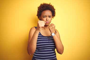 Beauitul Afro-Amerikalı kadın izole edilmiş sarı arka plan üzerine yaz tişörtü giyiyor. Yumruk yumruğa, agresif ve öfkeli saldırı, tehdit ve şiddet.