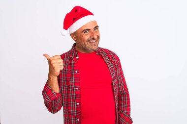 Noel Baba şapkası takan orta yaşlı bir adam izole edilmiş beyaz arka planda gülümseyen ve baş parmağıyla yüzünü gösteren bir gülümseme ile duruyor..