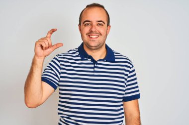 Sıradan çizgili polo giyen genç adam izole edilmiş beyaz arka planda duruyor gülümsüyor ve kendine güvenen el hareketleriyle küçük boy işareti yapıyor parmaklarıyla ve kamerayla bakıyor. Ölçü kavramı.