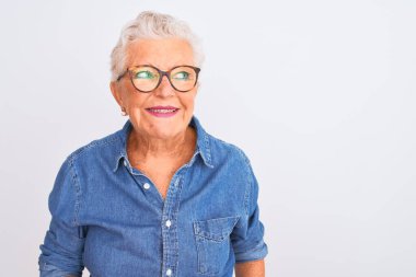 Yaşlı, gri saçlı, kot gömlek ve gözlüklü bir kadın izole edilmiş beyaz arka planda gülümsüyor ve diğer tarafa bakıyor..