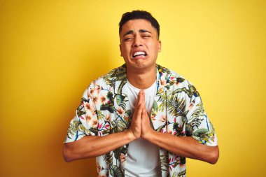 Tatilde olan genç Brezilyalı bir adam, izole edilmiş sarı arka planda çiçekli bir gömlek giyiyor. Yüzünde umut ifadesi olan ve endişeli bir şekilde el ele yalvarıyor ve dua ediyor. Af diliyor. Din kavramı.