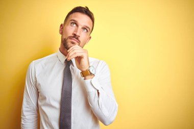 Sarı izole arka planda zarif beyaz gömlek giyen yakışıklı bir iş adamı. Elleri çenesinde soru sorarken, düşünceli bir ifade takınıyor. Düşünceli bir yüzle gülümsüyor. Şüphe kavramı.