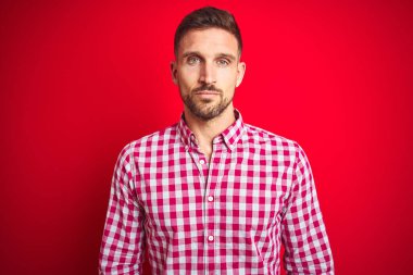 Kırmızı izole edilmiş arka plan üzerinde genç yakışıklı bir adam. Yüzünde ciddi bir ifadeyle rahatlamış. Basit ve doğal bir şekilde kameraya bakıyorsun..