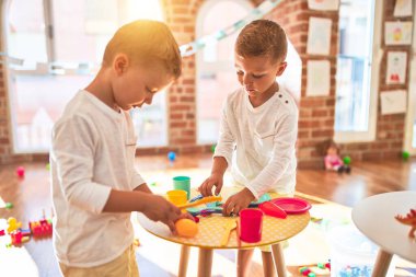 Adorable blonde twins playing around lots of toys. Cooking plastic food toy at kindergarten
