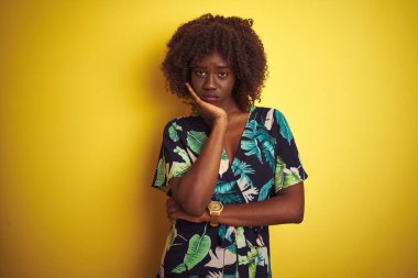 Sarıya boyanmış çiçekli bir elbise giyen Afrikalı genç bir kadın kollarını kavuşturup depresyondan sıkılmış ve yorgun göründüğünü düşünüyor..