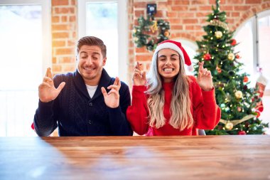 Noel Baba şapkası takan genç bir çift Noel ağacının etrafındaki sandalyeye ve masaya oturmuş umut ve gözlerin kapalı bir şekilde gülümseyerek el sallıyor. Şans ve batıl inanç..