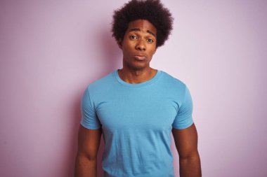 Afro saçlı, mavi tişörtlü Afro-Amerikalı bir adam, izole edilmiş pembe arka planda dikiliyor. Depresyonda ve endişe içinde, kızgın ve korkmuş bir şekilde ağlıyor. Üzücü ifade.