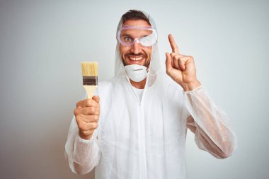 Profesyonel işçi ekipmanı giyen ressam arka planda fırça tutarken bir fikre ya da soru işaretine şaşırdı.
