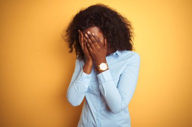 Afro-Amerikalı iş kadını zarif bir gömlek giyerek izole edilmiş sarı arka plan ve ağlarken suratını ellerle kapatan üzgün bir ifade. Depresyon kavramı.