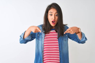 İzole edilmiş beyaz arka plan üzerinde çizgili tişört ve kot giyen genç Çinli kadın parmaklarını göstererek reklamını yapıyor, şaşırmış yüzünü ve ağzını açıyor.