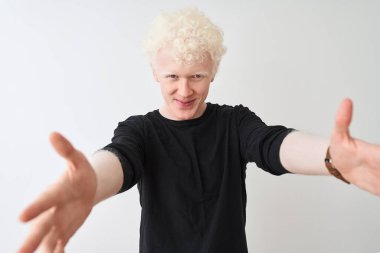 Siyah tişörtlü genç albino bir adam izole edilmiş beyaz arka planda dikiliyor ve kameraya sarılıp gülümsüyor. Mutluluğu kucaklayan neşeli bir ifade..