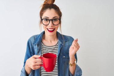 Young beautiful redhead woman drinking cup of coffee over isolated white background screaming proud and celebrating victory and success very excited, cheering emotion