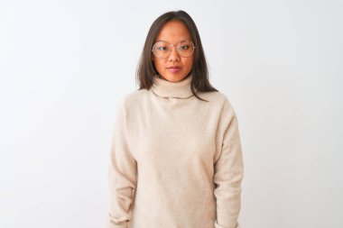 Balıkçı yaka kazak ve gözlük takan genç Çinli kadın izole edilmiş beyaz arka plan üzerine rahatlamış ve yüzünde ciddi bir ifadeyle rahatlamış. Basit ve doğal bir şekilde kameraya bakıyorsun..