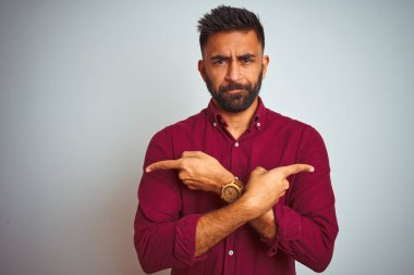 İzole edilmiş gri arka planda duran kırmızı şık tişörtlü genç Hintli adam iki tarafı da işaret ediyor, farklı yönler farklı.