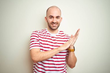 Sakallı genç ve kel bir adam, beyaz izole edilmiş arka planda sıradan kırmızı tişörtler giyiyor, mutlu ve neşeli alkışlıyor, gururla gülümsüyor.