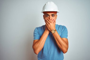 Güvenlik kaskı takan genç Brezilyalı mühendis izole edilmiş beyaz arka planda dikiliyor ağzını yanlışlıkla ellerle kapatıyor. Gizli konsept.
