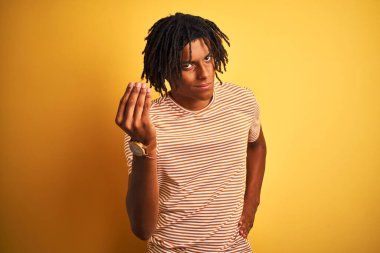 Rastalı tişörtlü Afro adam izole edilmiş sarı arka planda duruyor. İtalyan jestleri yapıyor. Elleri ve parmakları kendinden emin ifade ediyor.