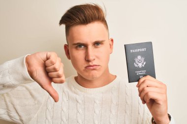 Amerika Birleşik Devletleri pasaportu taşıyan genç yakışıklı bir adam öfkeli yüzüyle izole edilmiş beyaz bir arkaplan, olumsuz işaret baş parmakları aşağıda, reddedilme konsepti.