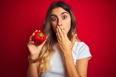 Kırmızı arka planda biber tutan güzel bir kadın. Ağzı kapalı. Utanç verici bir hata, korku ifadesi, sessizlikten korkmak, gizli bir kavram.