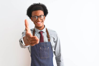 İzole edilmiş beyaz arka planda önlük takan Afro-Amerikan esnaf dostça bir selamlama ve hoş geldin hediyesi olarak gülümsüyor. Başarılı bir iş..