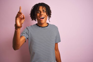 Rasta saçlı, lacivert tişörtlü, izole edilmiş pembe arka planda duran Afro adam başarılı bir fikri işaret ediyor. Heyecanlı ve mutlu. Bir numara..