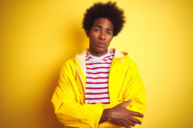 Siyah saçlı Afro-Amerikalı bir adam izole edilmiş sarı arka plan üzerinde duruyor şüpheci ve gergin, yüzünde çapraz kollu tasvip etmeyen bir ifade. Negatif kişi.