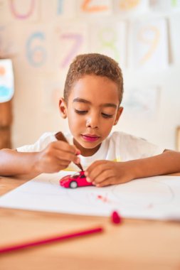 Güzel Afro-Amerikan çocuk. Anaokulunda masa başı kalem kullanarak araba oyuncağı boyuyor.